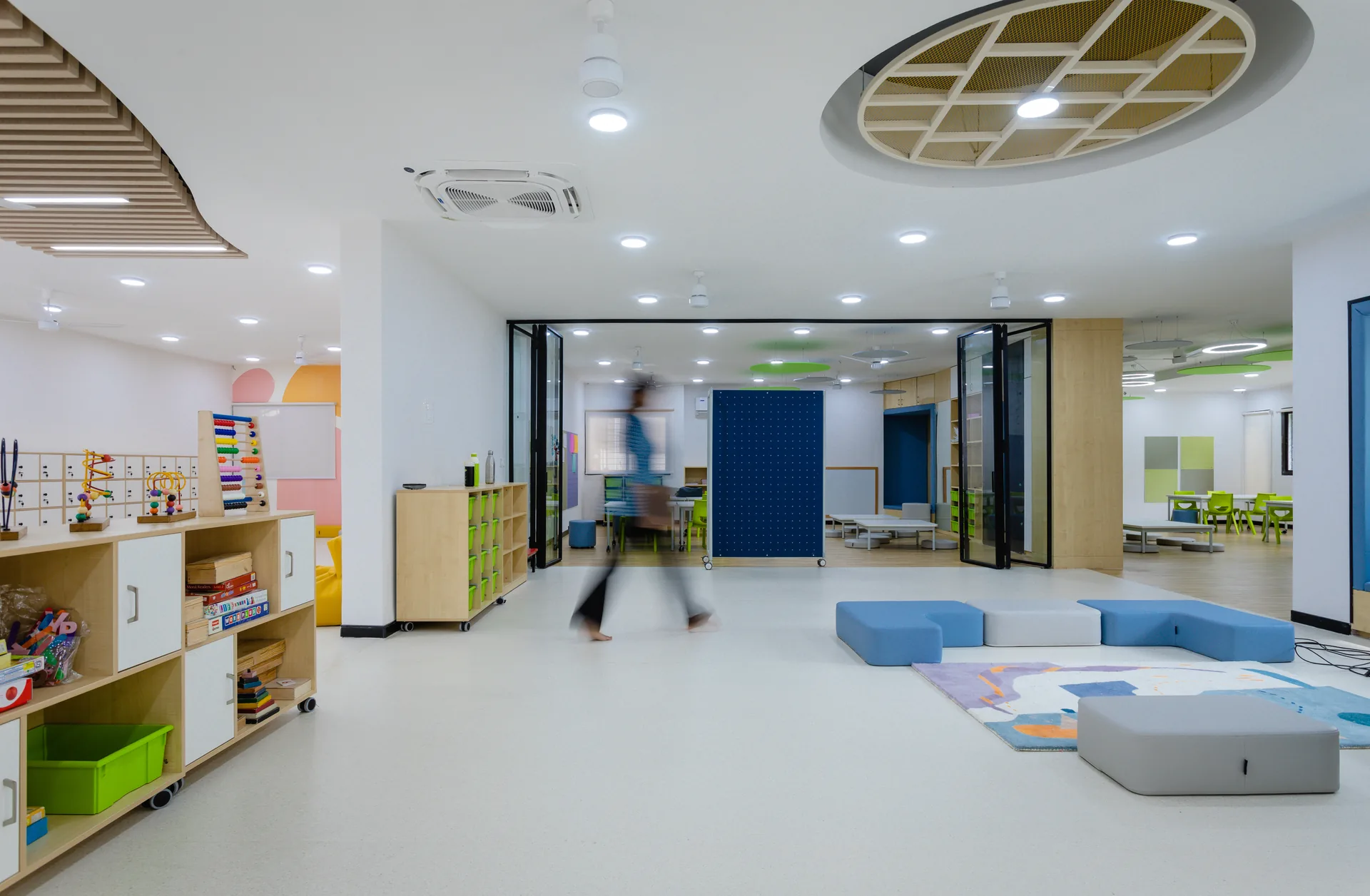 A vibrant common area featuring playful seating, integrated window niches, warm wooden ceiling details, and flexible open spaces designed to encourage interaction and informal learning.