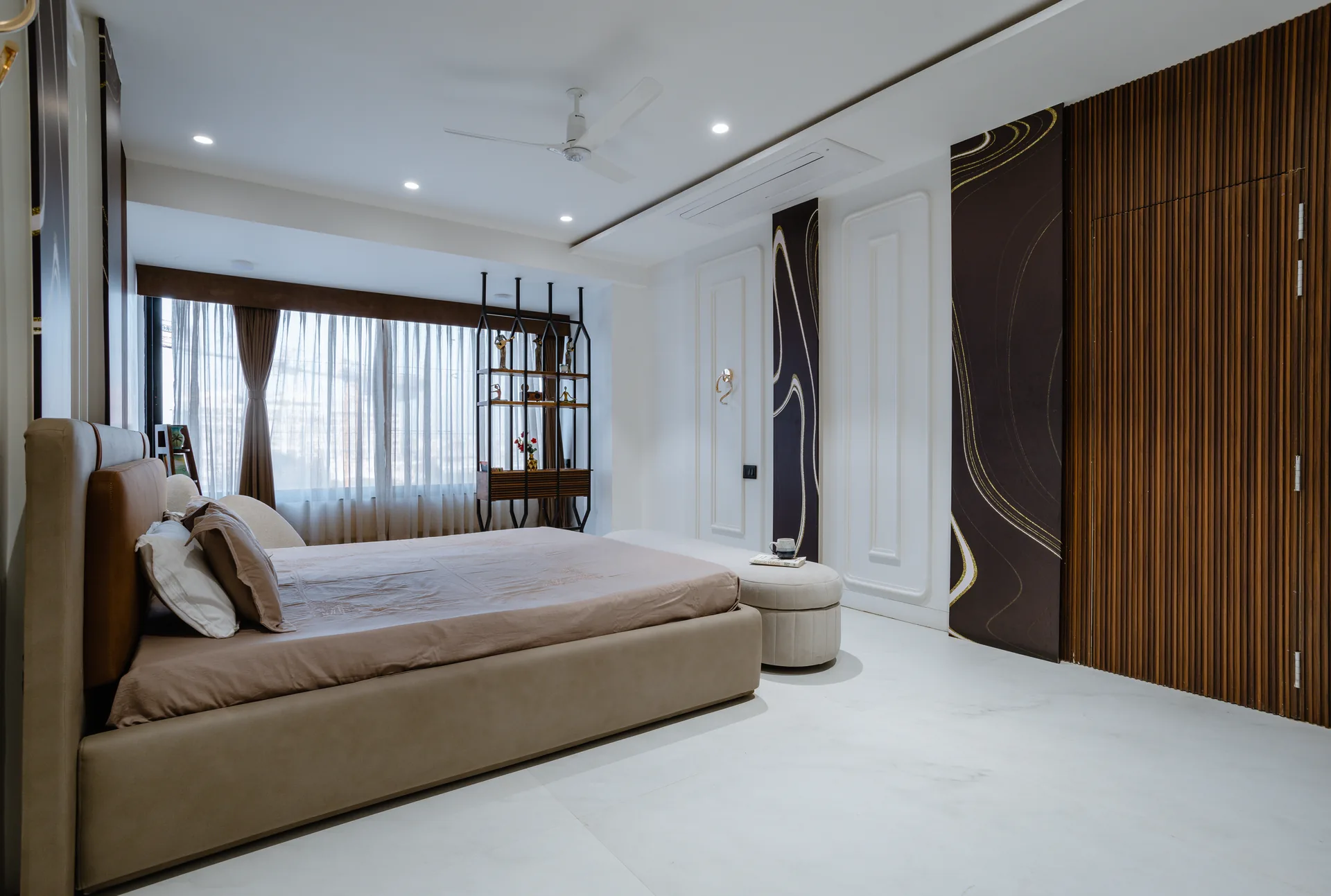 A sophisticated bedroom featuring soft neutral tones, elegant wall detailing, warm wooden accents, custom display shelving, and refined furniture, creating a calm and luxurious retreat.