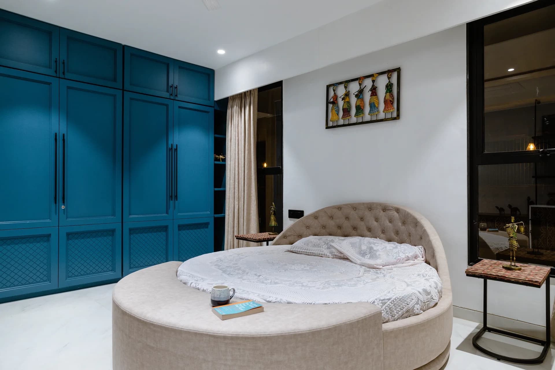 A vibrant bedroom featuring bold blue wardrobes, intricate patterned cabinetry, warm wooden accents, and minimal décor, creating a fresh contemporary space with distinctive traditional character.