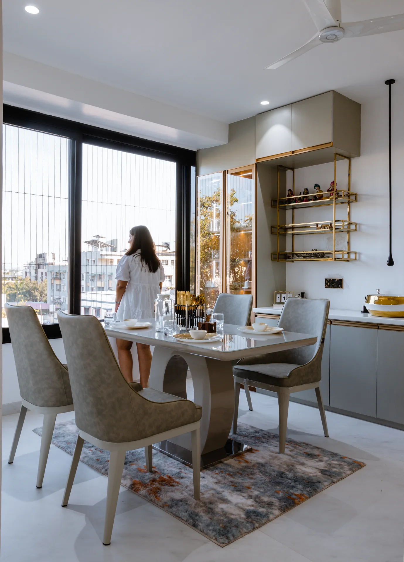 An elegant dining space featuring sleek furniture, open display shelving, warm metallic accents, and abundant natural light, creating a sophisticated setting for everyday dining and gatherings.