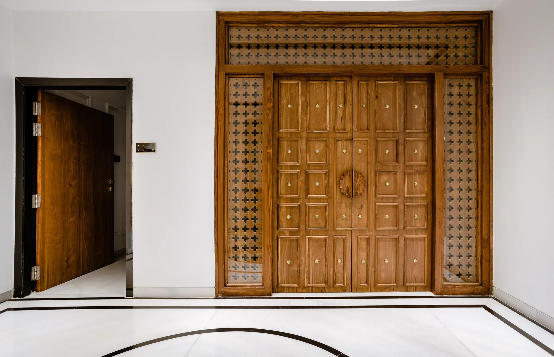 A statement living room featuring rich red seating, intricate wooden craftsmanship, traditional motifs, and elegant wall detailing, creating a warm space rooted in timeless Indian character.